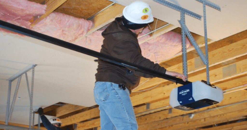 Worker installs Raynor opener on ceiling beams.